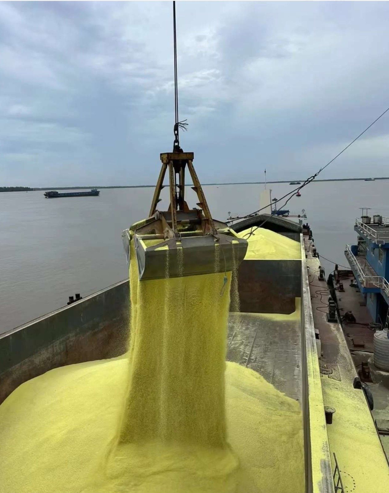 Grab crane loading granular sulphur into a vessel hold